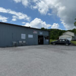 Front of B&G Pro Shop, a gray metal building with signs, chairs outside, and a car parked on a gravel lot.