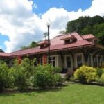 Coal Heritage Trail Interpretive Center with a red metal roof, wide overhangs, and cream-colored walls, surrounded by landscaped bushes and a grassy lawn under a partly cloudy sky.