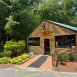 Buffalo Trail Restaurant, a rustic log-style building with a green roof and landscaped entrance, surrounded by trees.