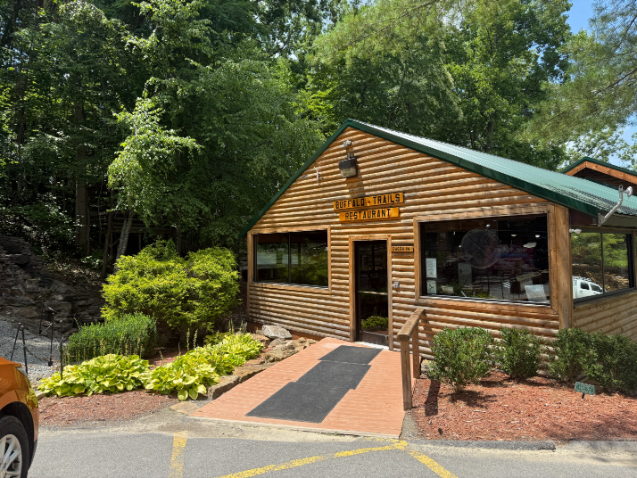 Buffalo Trail Restaurant, a rustic log-style building with a green roof and landscaped entrance, surrounded by trees.