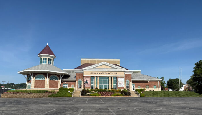 Front view of the Chuck Mathena Center, a large brick performing arts venue with large windows and columns, seen from the parking lot.