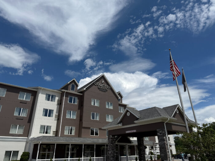 Front of the Country Inn & Suites in Princeton, a multi-story brown and cream building with a peaked roof entrance, American flag, and a covered drop-off area.