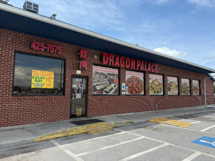Exterior of the Dragon Palace, a brick building with bold red lettering, food photos displayed along the windows, and a sign advertising a $12 all-you-can-eat buffet.