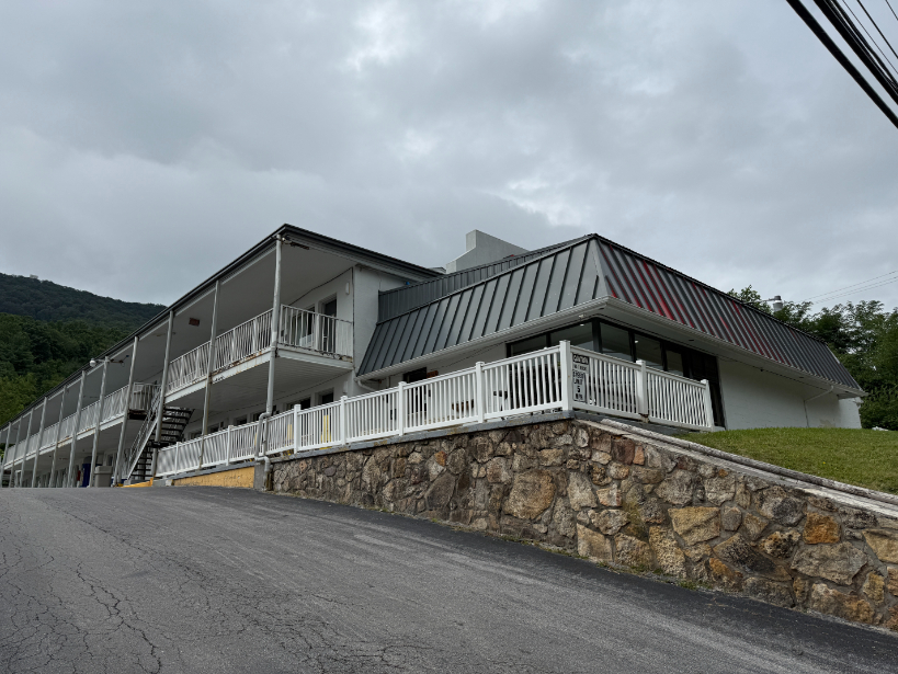 Econo Lodge motel with a two-story white exterior, metal roof, long balcony areas, and white railing, set on a slope with a stone retaining wall.