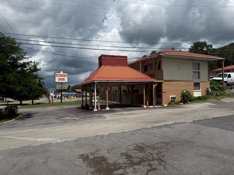 Economy Inn with a red roof and covered entrance, located near a roadside sign under a cloudy sky.