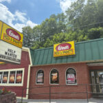 Exterior of Gino's Pizza & Spaghetti, a brick restaurant with a green roof and large yellow sign, next to a signboard advertising jobs.