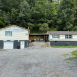 Hillbilly Hideaway lodging with two connected buildings, a gravel lot, and a forested hillside in the background.