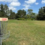 A disc golf course sits on a field in a green field inside a park.
