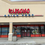 Front of Kimono Asian Food restaurant in a shopping plaza, with large red and blue signage above the entrance and mural-style window art featuring landscapes and traditional attire.