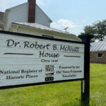 Sign for the Dr. Robert B. McNutt House, a historic 1840s home with light siding and a red brick chimney.