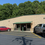 Exterior of Mountain Heritage Archery, a tan metal building with a green roof, nestled against a wooded hillside.