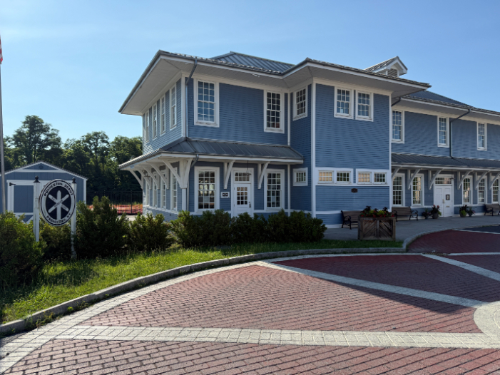 Blue, two-story Princeton Railroad Museum with white trim, large windows, and a covered front walkway with benches and flower planters.