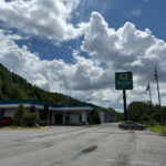 Quality Hotel and Conference Center in Bluefield, with a large parking lot, visible signage, and a backdrop of forested hills under a partly cloudy sky.