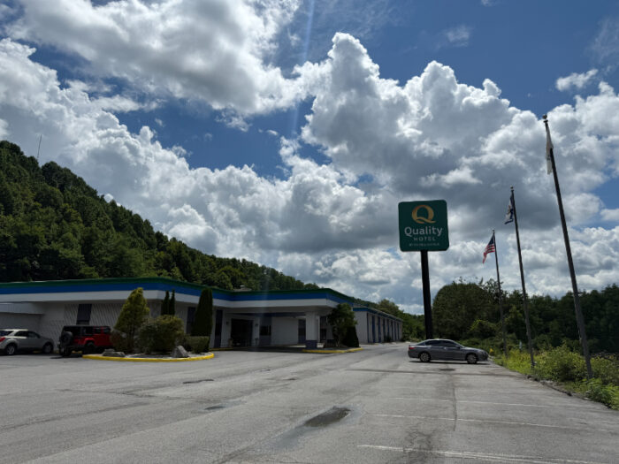 Quality Hotel and Conference Center in Bluefield, with a large parking lot, visible signage, and a backdrop of forested hills under a partly cloudy sky.