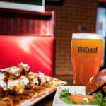 Food and drink at The Railyard Restaurant, featuring chicken and waffle nachos, a cheeseburger, and a pint of beer in a branded glass.