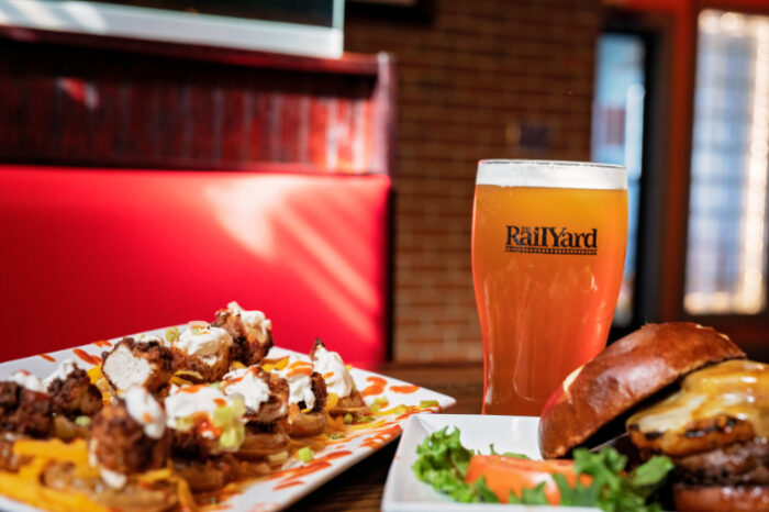 Food and drink at The Railyard Restaurant, featuring chicken and waffle nachos, a cheeseburger, and a pint of beer in a branded glass.