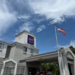Exterior of Sleep Inn & Suites in Princeton, a light gray building with a tower sign, arched entrance canopy, and two flagpoles flying the American and West Virginia flags.