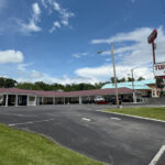Exterior of the Turnpike Motel in Princeton, a single-story building with a red roof, parking spaces out front, and a large roadside sign.