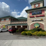 The Willow Gift Gallery in a large brick and tan building with a green roof, windows, and a corner tower featuring a clock. A UPS Store sign is also mounted on the tower.