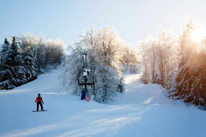 Snowboarder gliding down a sunlit slope at Winterplace Ski Resort, surrounded by snow-covered trees and a ski lift in the background.