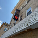 Exterior of Diamonds N' Gold Look, showing a vertical black and red sign on a brick building with white shingle awning.