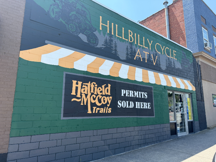 Hillbilly Cycle ATV storefront with a green and yellow striped mural advertising Hatfield-McCoy Trail permits.