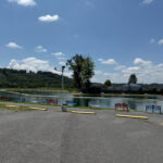 A peaceful fishing pond with colorful benches along the edge, surrounded by wooded hills and a blue sky.