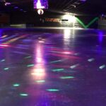 Colorful roller skating rink at The Skate Shack, illuminated by vibrant neon lights reflecting off the floor in a dark indoor space.