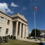 Stone government building with tall columns, an American flag on a pole, and a historic cannon on the lawn in front of the Mercer County War Museum in Princeton, West Virginia