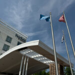 Flags flying in front of Fairfield Inn by Marriot, with the hotel name and the top of the building in view.