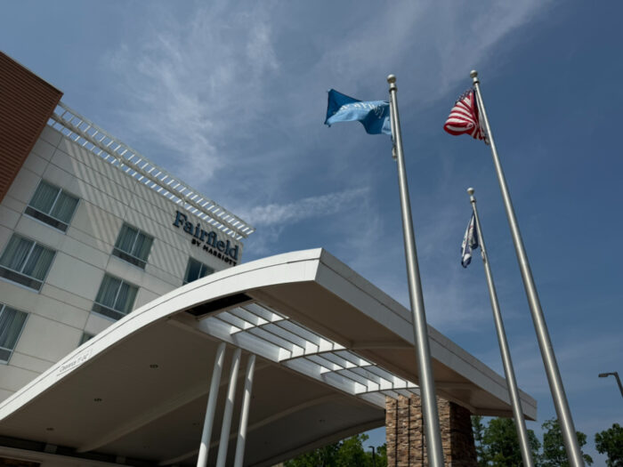 Flags flying in front of Fairfield Inn by Marriot, with the hotel name and the top of the building in view.