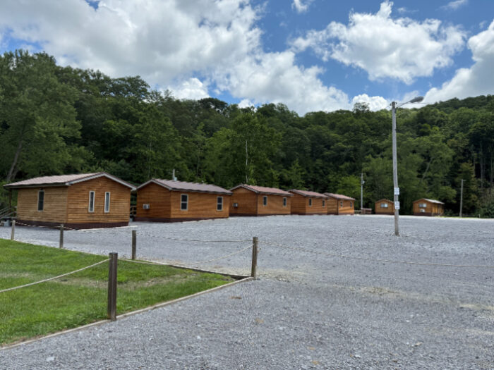 Mud Pit ATV Resort featuring a row of wooden cabins on a gravel lot, surrounded by trees under a partly cloudy sky.