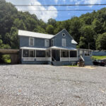 Busted ATV Resort, a light blue two-story house with a covered porch and gravel parking area, set against a wooded hillside.