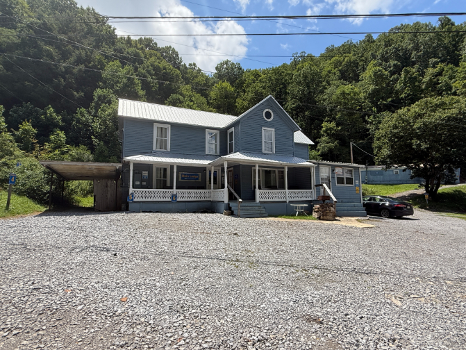 Busted ATV Resort, a light blue two-story house with a covered porch and gravel parking area, set against a wooded hillside.