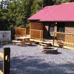 Trailhead Inn, a log cabin style accommodation with gravel area containing a firepit, a wood porch, and red roof.