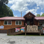 Front of Old School Grocery and Grill, a rustic wooden building with a red roof, ramp entrance, and signs displayed on porch.