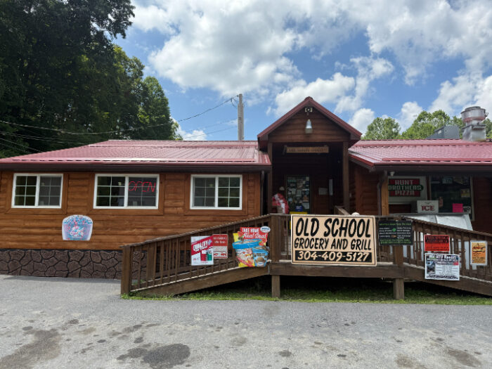 Front of Old School Grocery and Grill, a rustic wooden building with a red roof, ramp entrance, and signs displayed on porch.