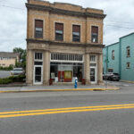A two-story brick building with tall windows and decorative stone columns, housing Holler: Contemporary Art Gallery, located on a corner street spot.
