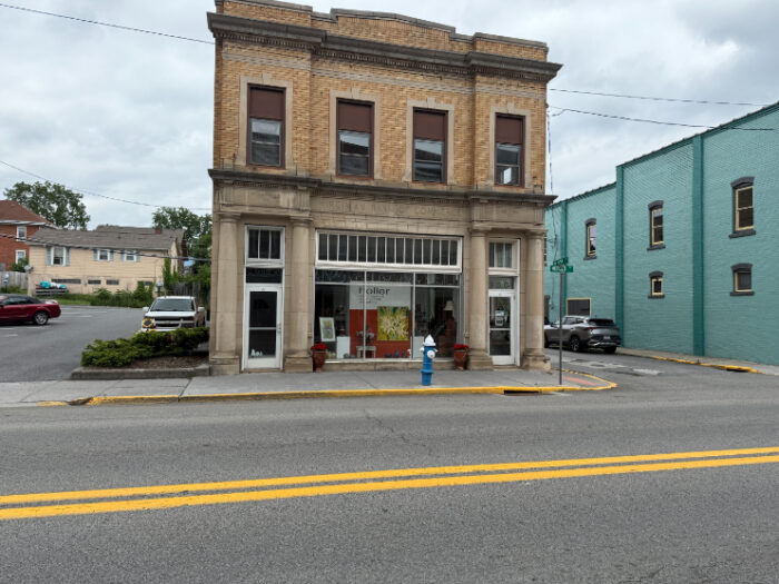A two-story brick building with tall windows and decorative stone columns, housing Holler: Contemporary Art Gallery, located on a corner street spot.