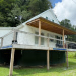 Coal Miner's Hideout, a white cabin-style rental with a covered porch and elevated wooden deck set against a wooded hillside.