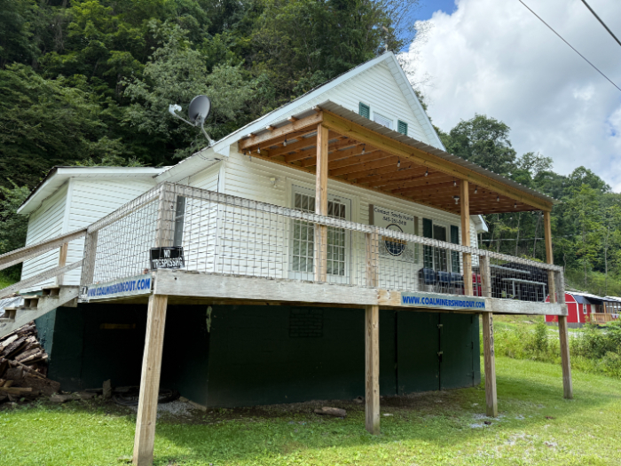 Coal Miner's Hideout, a white cabin-style rental with a covered porch and elevated wooden deck set against a wooded hillside.