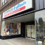 A storefront with a large sign reading 'Hammer and Stain DIY Workshop' above display windows that are filled with craft items, painted signs, and home decor.
