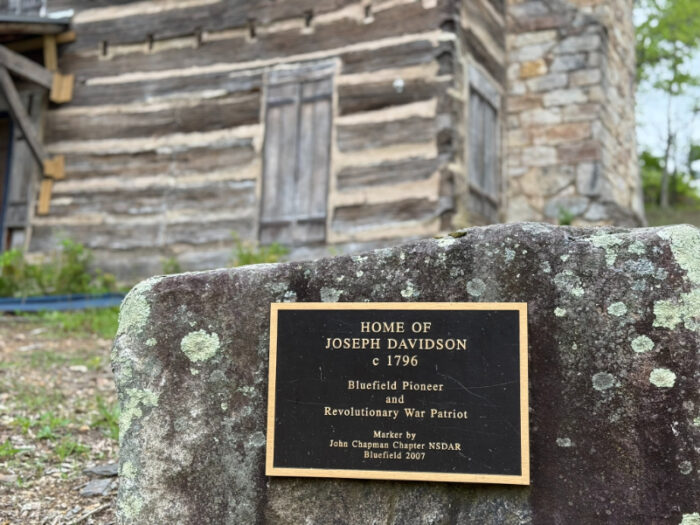Plaque on a moss-covered rock marking the home of Joseph Davidson, in front of a historic log and stone cabin.