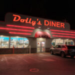 Dolly's Diner at night, featuring bold red neon trim, a retro-style sign, and large windows glowing with light from inside.