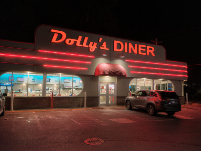 Dolly's Diner at night, featuring bold red neon trim, a retro-style sign, and large windows glowing with light from inside.