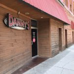 Entrance to Danny's Bar and Grill, with a wood-paneled exterior, a red overhang, and a black door beneath a bold red and white sign.
