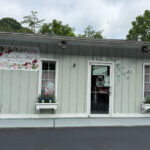 Sweet Pea Hill Boutique storefront with floral signage, pastel green siding, and window boxes with plants and small American flags.
