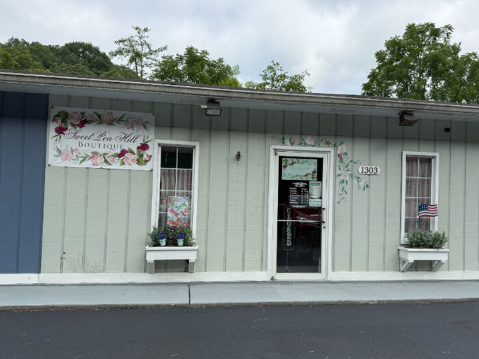 Sweet Pea Hill Boutique storefront with floral signage, pastel green siding, and window boxes with plants and small American flags.