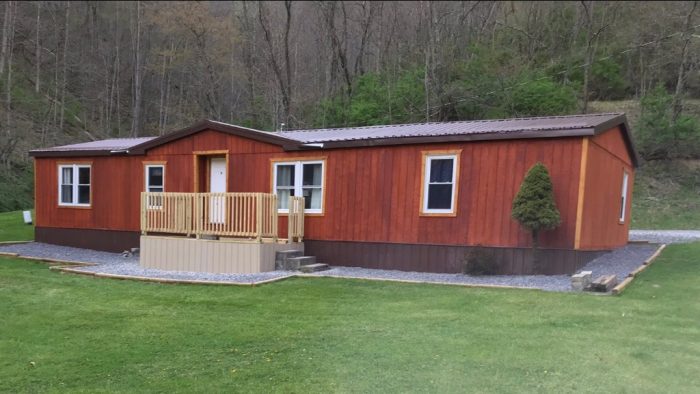 Red single-story building with a front deck and white-trimmed windows at Twin Springs ATV Park and Campground, set beside a large grassy lawn with trees in the background.