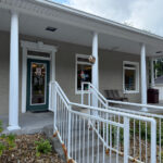 Exterior of Sweet Thingz storefront with white columns, a front ramp with railings, and a glass door displaying business hours.